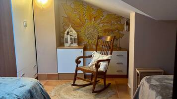 Une chambre avec deux lits, un fauteuil à bascule, une fresque murale et une petite table.