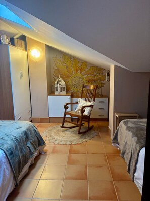 Een slaapkamer met twee bedden, een schommelstoel, een muurschildering en een klein tafeltje.