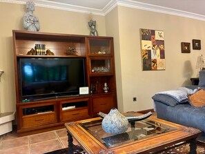 Een woonkamer met een grote flatscreen televisie, een houten entertainmentkast en een blauwe bank.