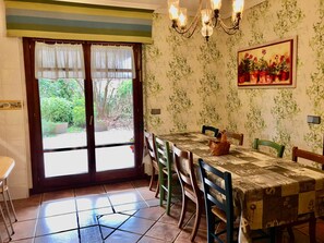 Un coin repas avec une table dressée pour quatre personnes, entourée de chaises, d’un lustre et d’une fenêtre agrémentée de rideaux.