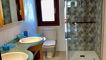 A bathroom with two sinks, a toilet, a shower, and a window.