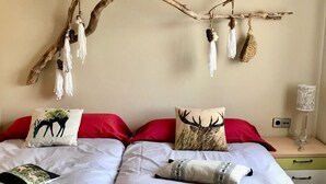 Een slaapkamer met twee bedden, elk met een ander kussenontwerp, een tak met hangende decoraties, en een nachtkastje met een lamp.