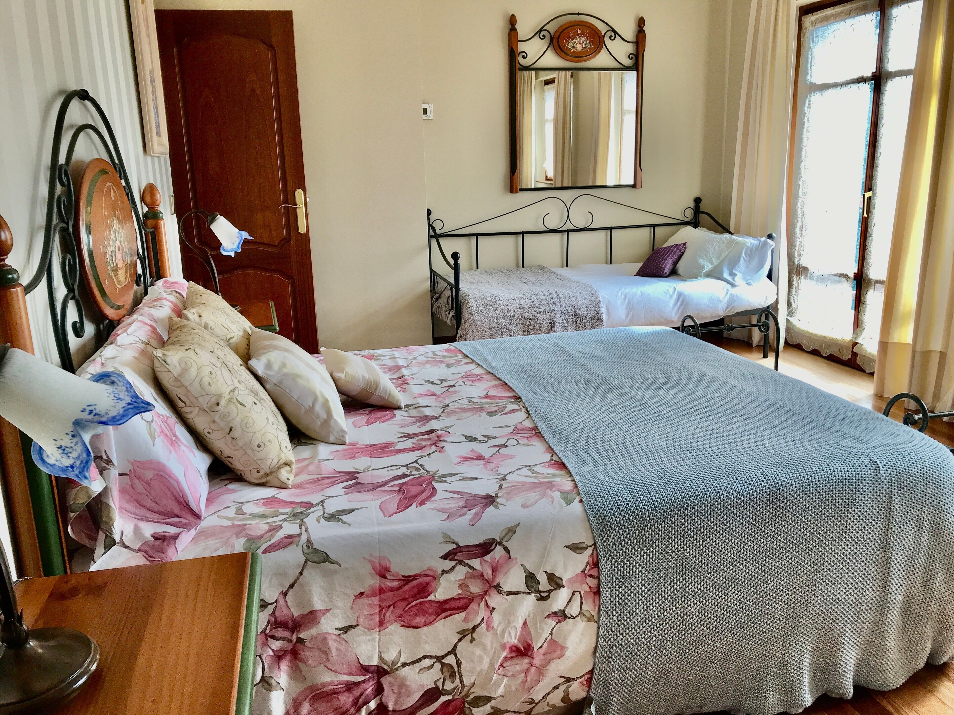 A bedroom with two beds, a wooden door, a mirror, and a window with curtains.
