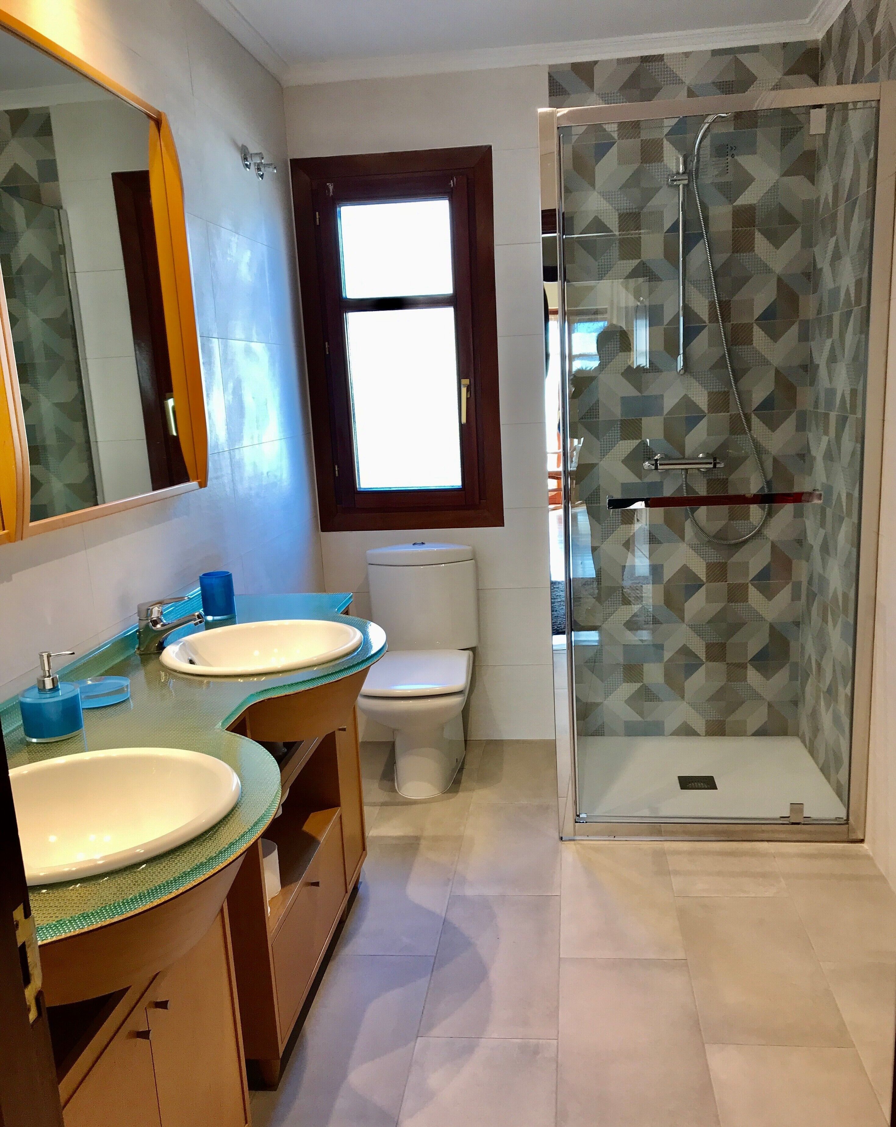 Un baño con dos lavamanos, un inodoro y una ducha con mampara de cristal.