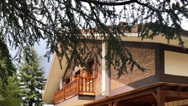Een gebouw met twee verdiepingen, een gevel van natuursteen, een houten balkon en een terras.
