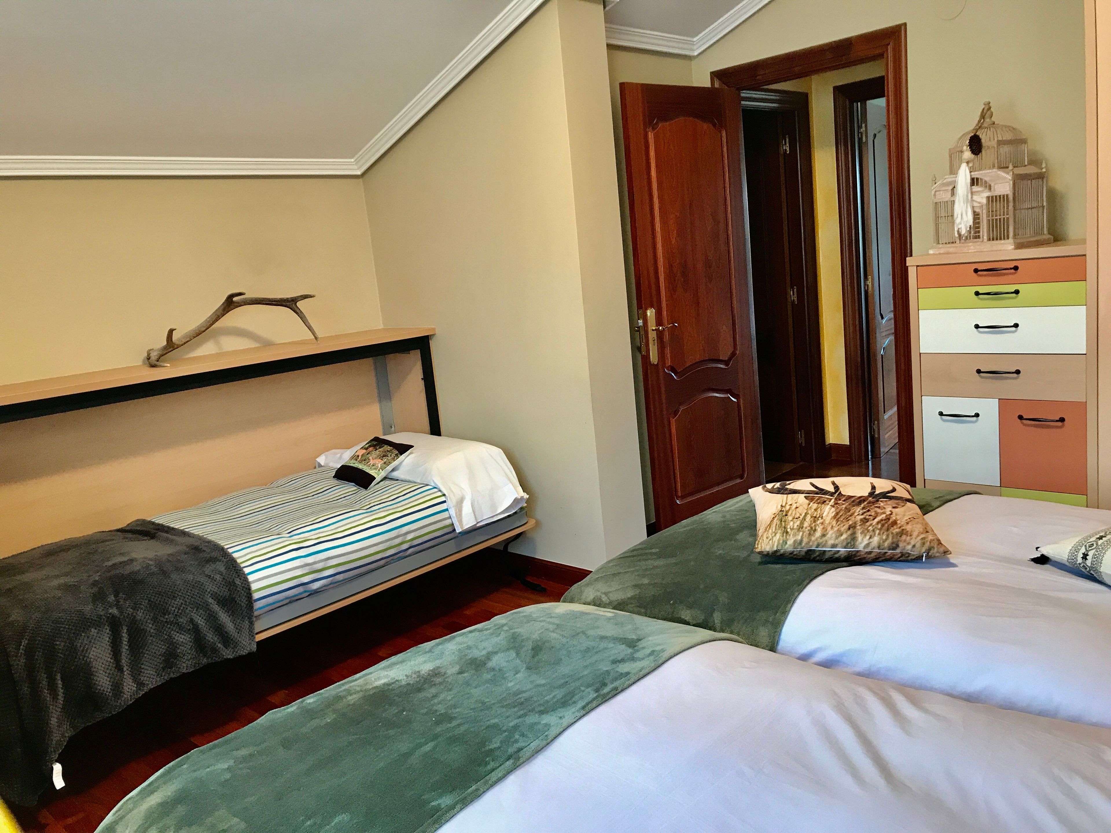 Une chambre à coucher avec un lit superposé, un lit simple, une porte en bois et une commode dotée de plusieurs tiroirs.