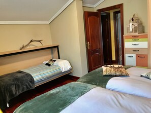 Une chambre à coucher avec un lit superposé, un lit simple, une porte en bois et une commode dotée de plusieurs tiroirs.