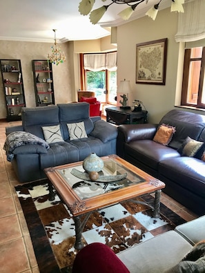 Ein Wohnzimmer mit einem blauen Sofa, einem Ledersofa, einem Glastisch und einem gemusterten Teppich.