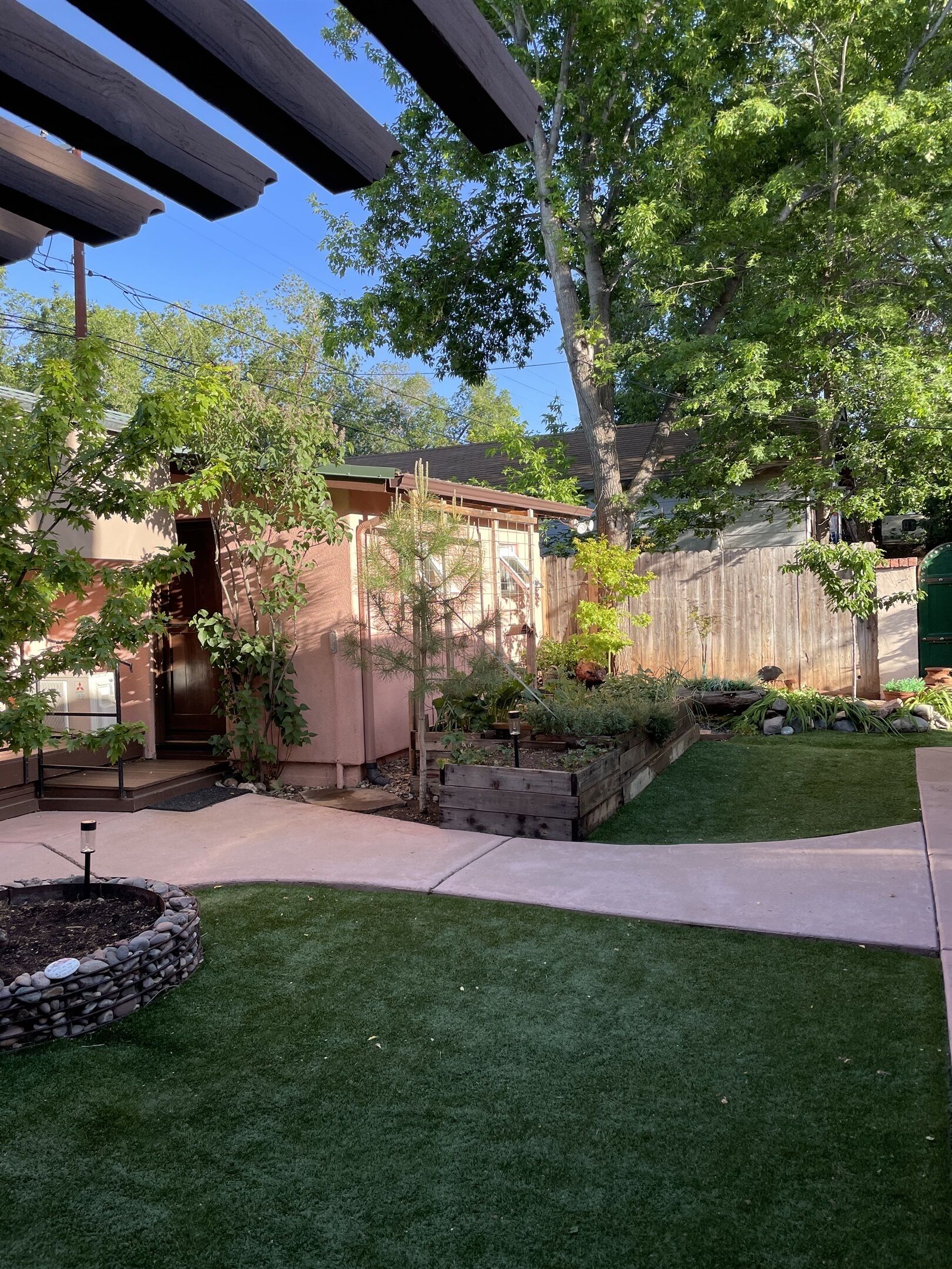 A backyard with a wooden deck, a brick house, a wooden fence, and a well-maintained lawn.