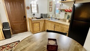 A compact kitchen with a wooden dining table, a refrigerator, and a small countertop. - The Pleasant Street Casitas: Queen Studio Suite (Prescott)