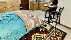 A compact bedroom with a bed, a ceiling fan, a kitchenette, and a dining area. - The Pleasant Street Casitas: Queen Studio Suite (Prescott)