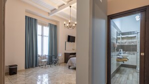 A hotel room with a bed, a desk, a chair, a TV, and a bathroom with a shower and sink. - Room 'Al Duomo - Camera King' with Shared Terrace, Wi-Fi and Air Conditioning (Licata)