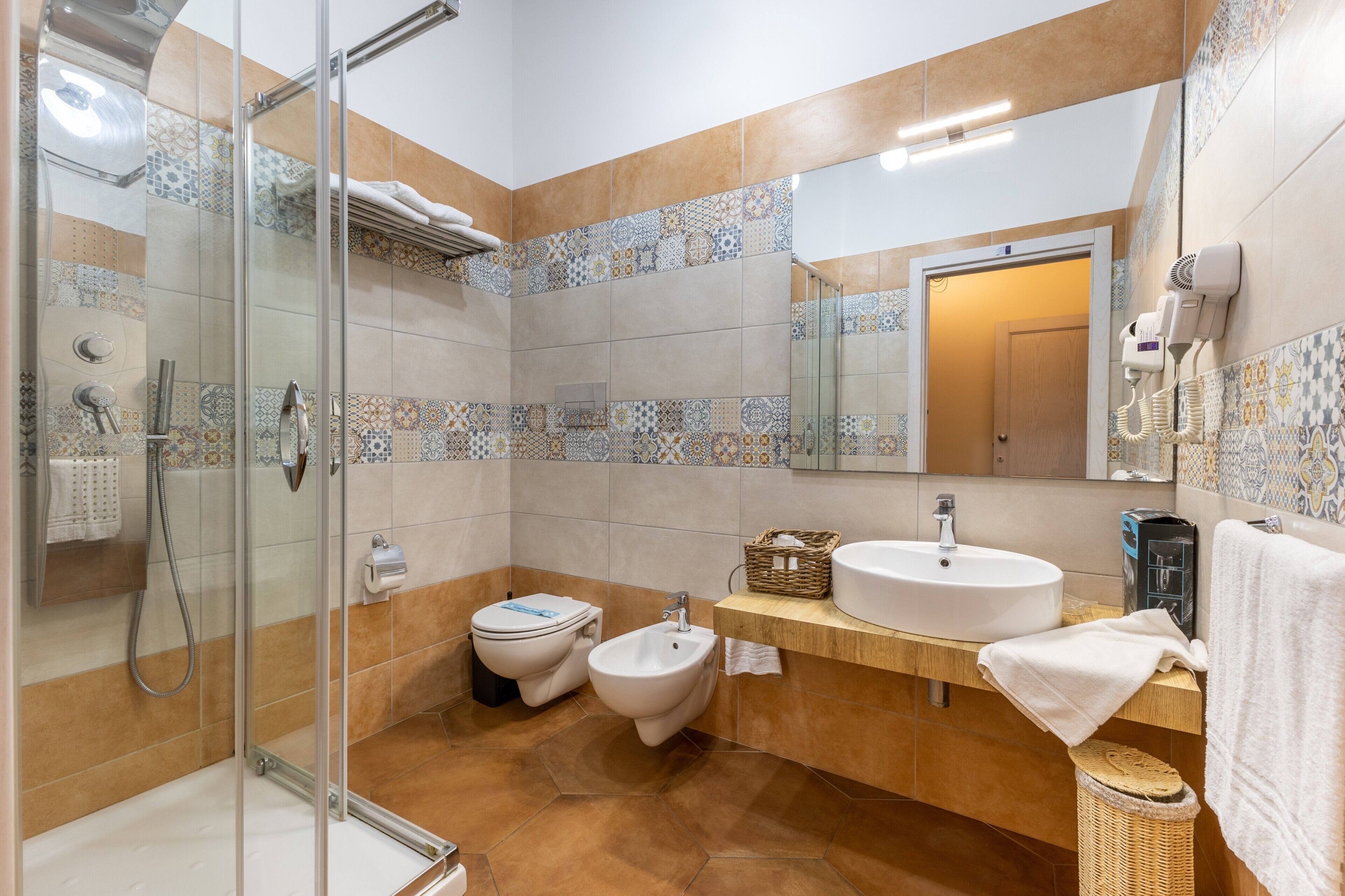 Une salle de bain équipée d’une douche, de toilettes, d’un bidet, d’un lavabo et d’un grand miroir.