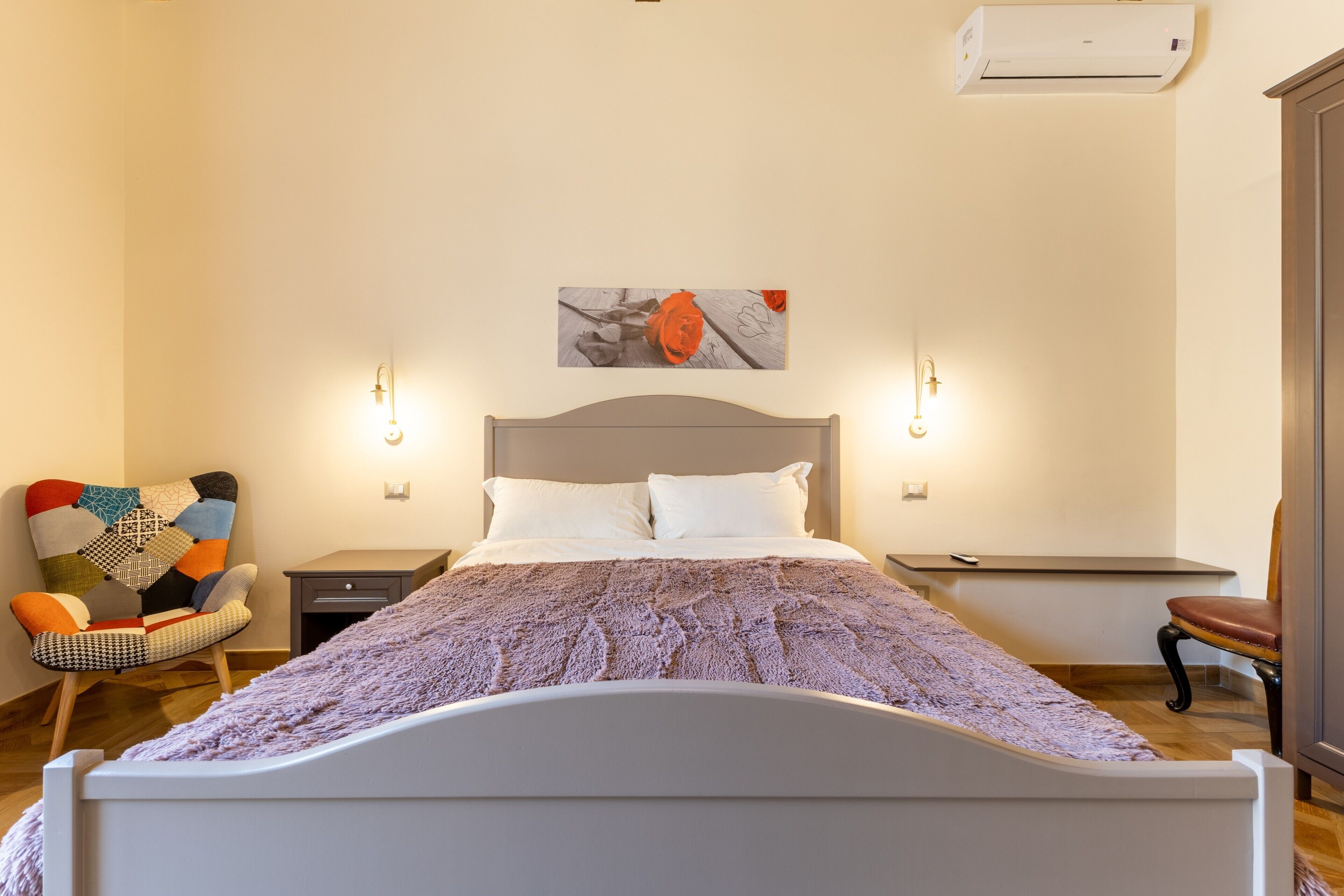 Une chambre à coucher comprenant un lit, une chaise, une table de chevet, une lampe et un climatiseur fixé au mur.