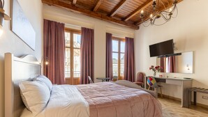 A bedroom with a bed, a desk, a chair, a TV, and a window with curtains.
