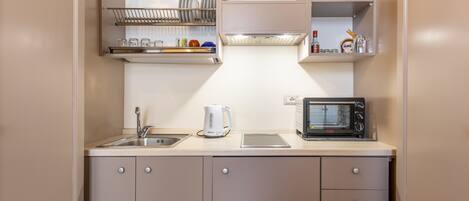 A compact kitchenette with a sink, kettle, microwave, and shelves for dishes and glasses.