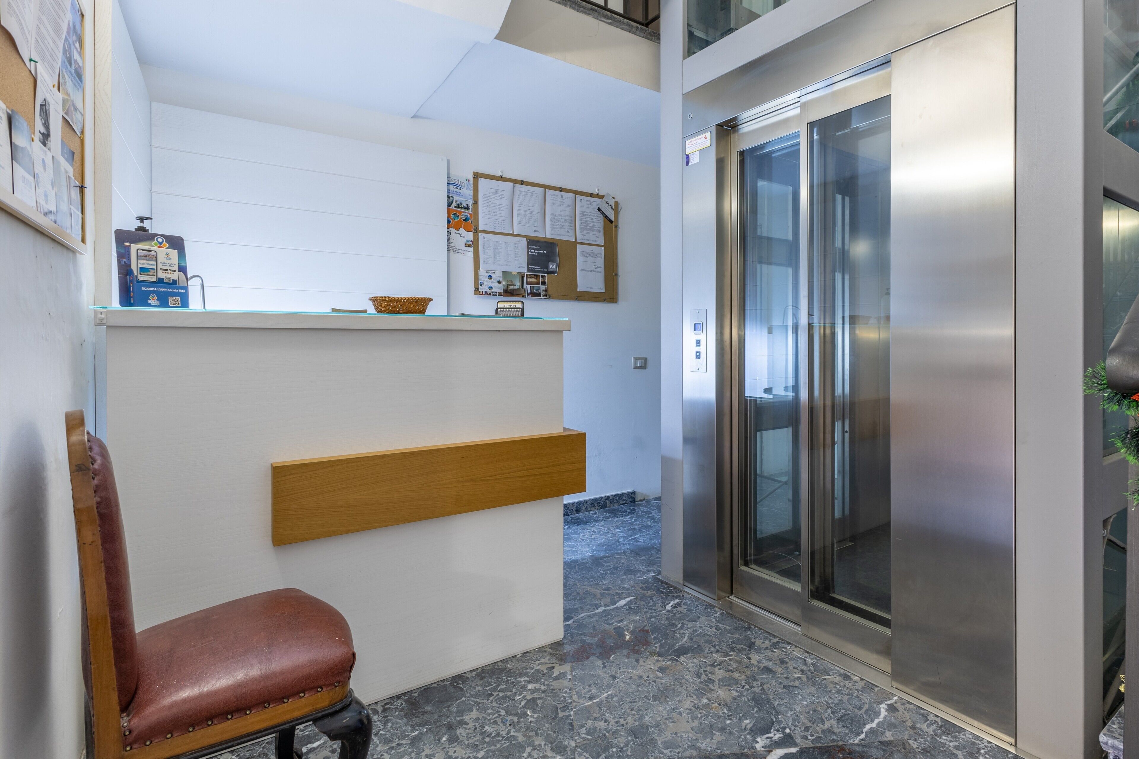 A reception area with a counter, a wooden bench, an elevator, and a marble floor.
