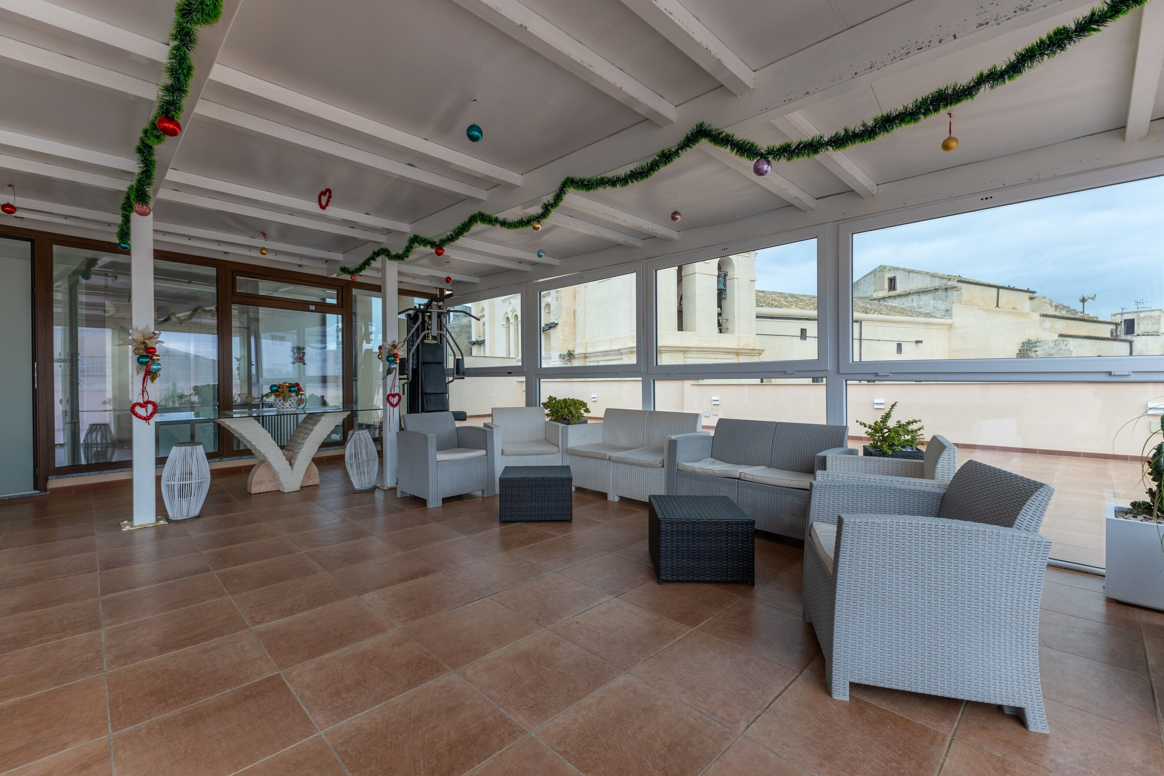 A spacious indoor area with wicker furniture, large windows, and a view of buildings outside.