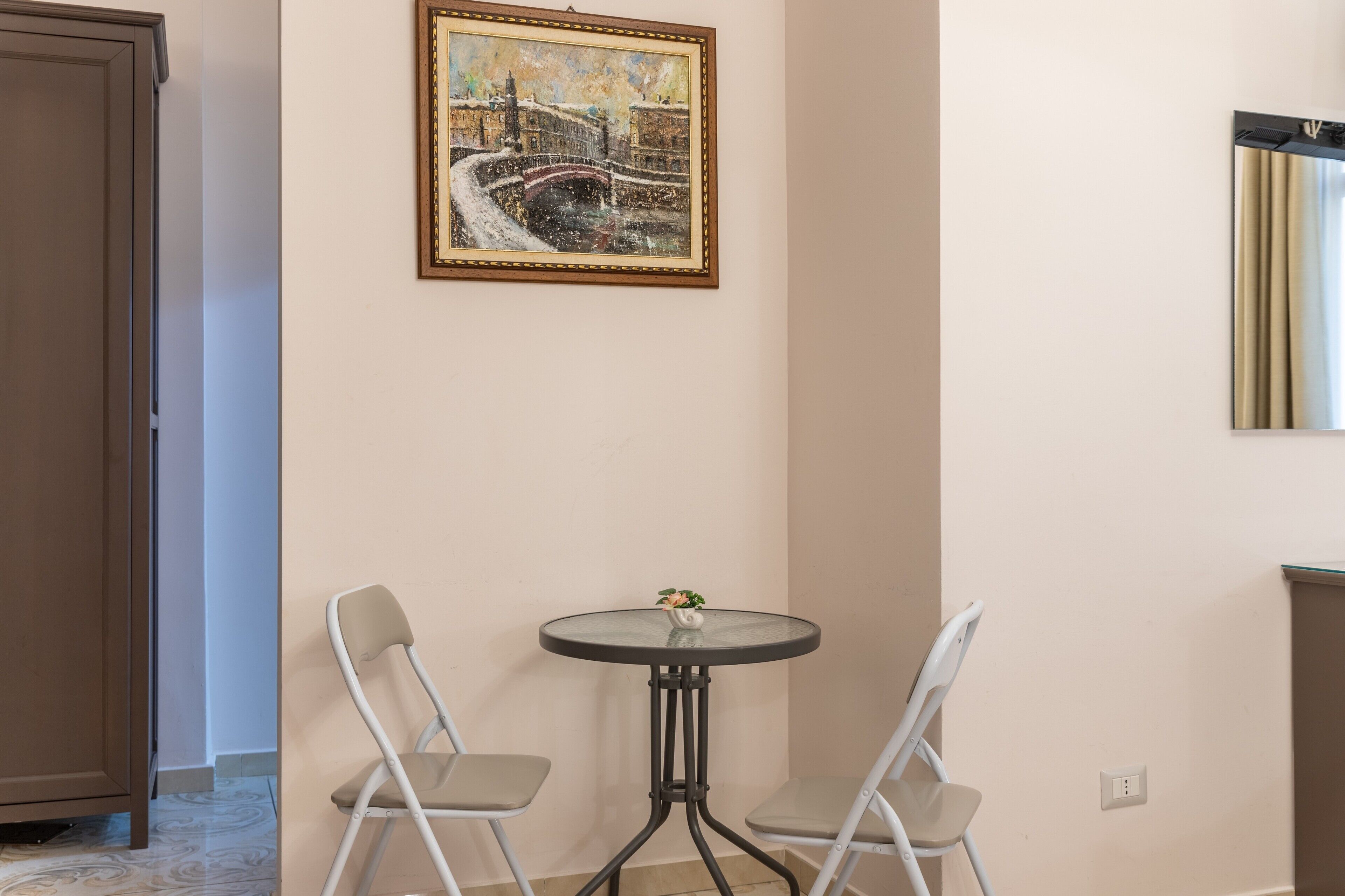 Une pièce avec une table ronde et deux chaises, un tableau au mur et une porte.