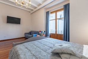 A bedroom with a bed, a television, a sofa, and a window with curtains. - Room 'Al Duomo - Suite' with Shared Terrace, Wi-Fi and Air Conditioning (Licata)