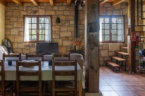 Una habitación con paredes de piedra, una mesa de comedor, sillas, una chimenea y una escalera.