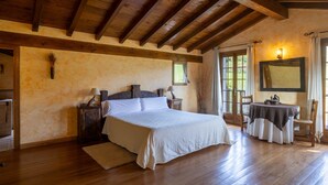 Een slaapkamer met een houten plafond, een bed met witte beddengoed, een nachtkastje, een tafel met tafelkleed en een spiegel aan de muur.