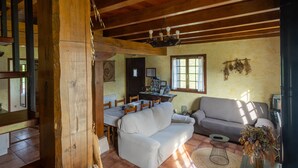Een rustiek interieur met houten plafond, een eethoek met tafel en stoelen, een bank en een raam met natuurlijk licht.