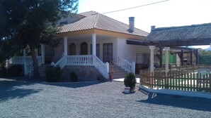 A two-story house with a tiled roof, a porch with white railings, and a fenced outdoor area.