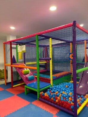 Un área de juegos con piscina de pelotas, toboganes y estructuras con red.