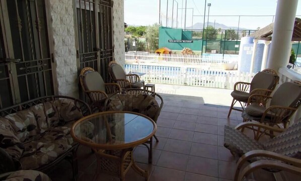 Un espacio de estar al aire libre cubierto con mobiliario de mimbre y una mesa de vidrio.