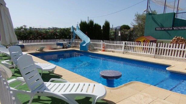 A swimming pool with a slide, white lounge chairs, and a fenced area.