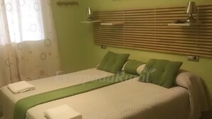 Una cama doble con una colcha verde y almohadas, una toalla blanca, un cabecero de madera y una ventana con cortina.