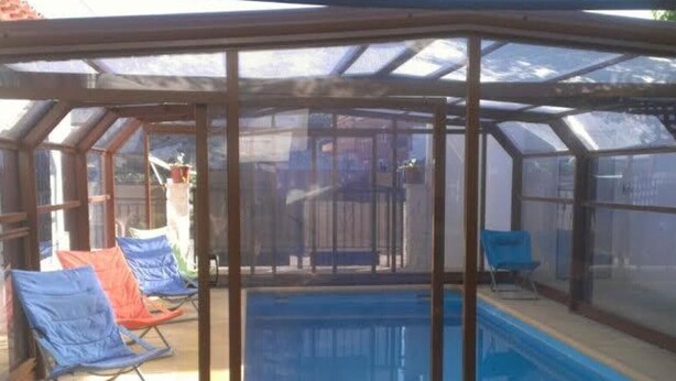 Un solárium con piscina, paredes de vidrio y una silla azul.