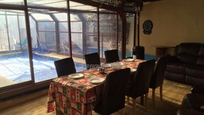 Un comedor con una mesa preparada para cuatro, una piscina visible a través de amplios ventanales y un reloj en la pared.