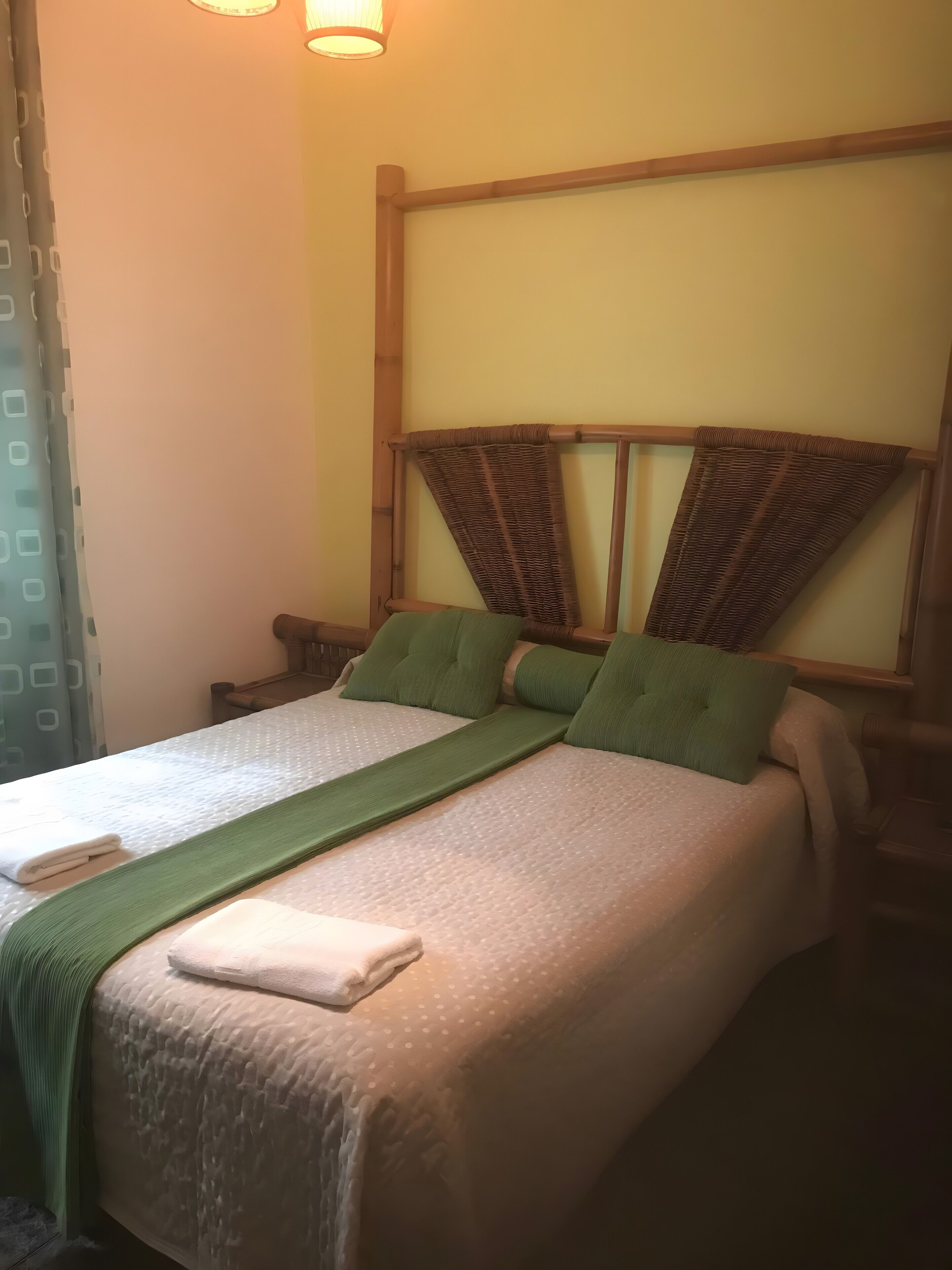 Una cama con una colcha verde, almohadas y una toalla doblada.