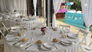 Runde Tische sind mit weißen Tischdecken, weißen Stühlen und Besteck gedeckt.