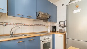 Una cocina compacta con armarios azules, un refrigerador de acero inoxidable, un horno empotrado y una cafetera.