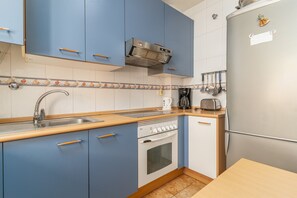 A compact kitchen with blue cabinets, a stainless steel refrigerator, a built-in oven, and a coffee maker. - Apartment 'Piso El Morche' with Shared Pool, Private Terrace and Wi-Fi (Torrox Costa)