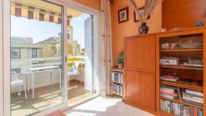 Habitación con puerta de vidrio corredera que da a un área exterior, una estantería de madera y una pequeña mesa con sillas.