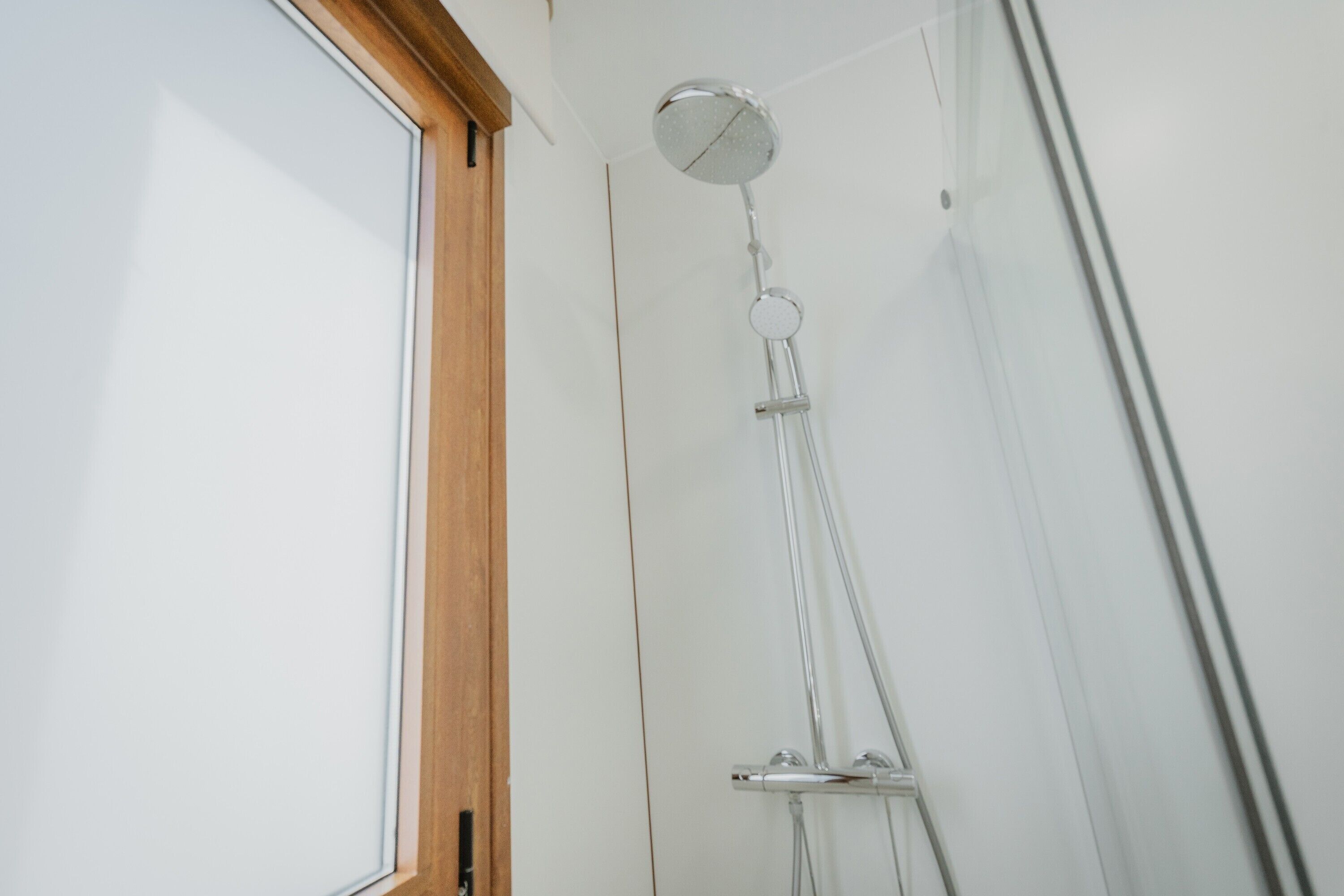 A shower with a glass enclosure and a wooden frame around the window.