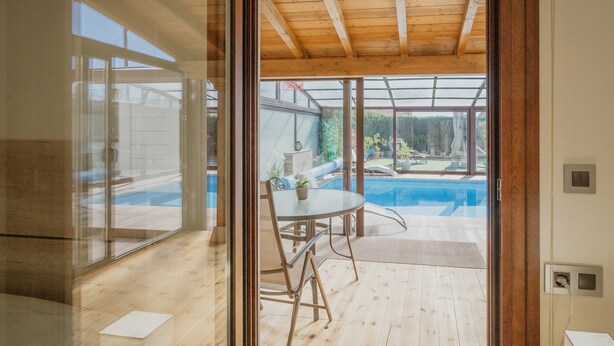 A modern interior with a wooden ceiling, a glass door leading to an outdoor area with a pool.
