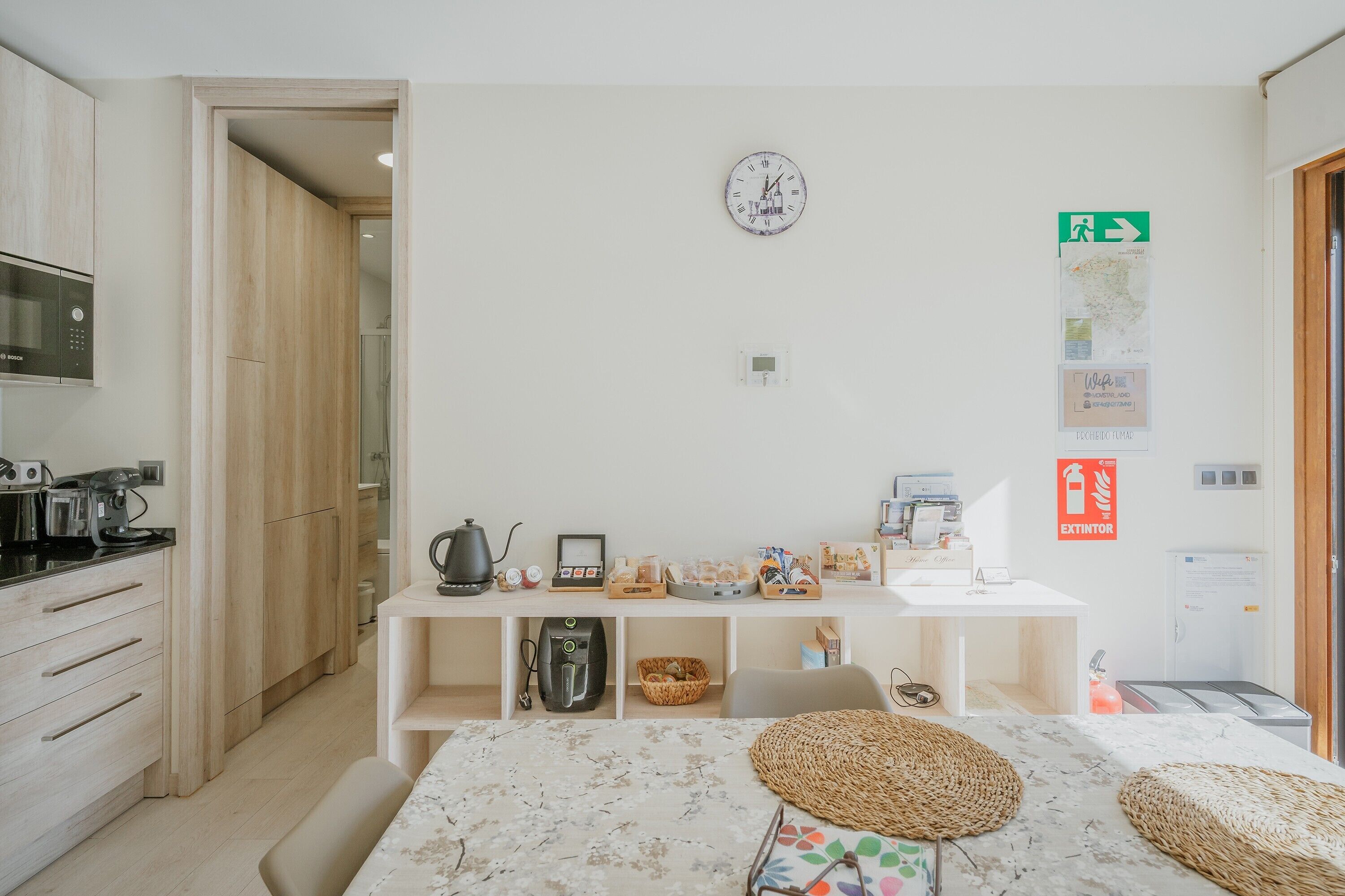 Una cocina moderna equipada con microondas, hervidor y cafetera, un comedor con mesa y sillas, y una pizarra en la pared.