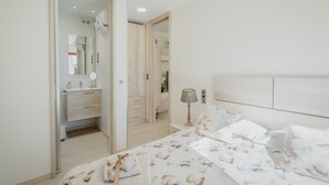A bedroom with a bed, a bedside table, a lamp, a mirror, a wardrobe, and a bathroom with a sink and mirror.