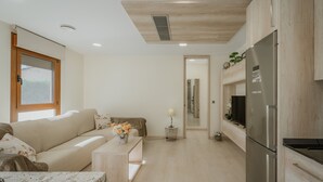 A modern living room with a sofa, a coffee table with flowers, a refrigerator, and a wooden ceiling.