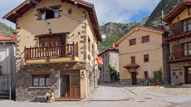 Un edificio tradicional con balcón, fachada de piedra y montañas al fondo.