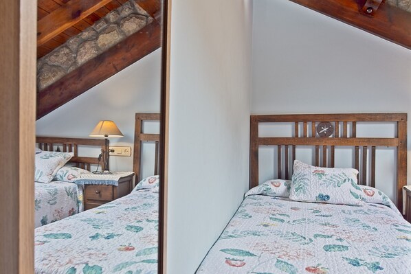 Un dormitorio con cabecera de madera, ropa de cama con estampado floral, una lámpara de noche y una mesita de noche.