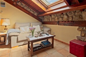 A cozy room with a stone wall, wooden beams, a sofa, a table with a lamp, and a red ottoman. - Eagle's Nest Country House in Picos de Europa with Mountain Views (Portilla de la Reina)