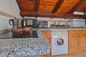 A kitchen with granite countertops, a coffee maker, a microwave, a toaster, a washing machine, wooden cabinets, and a tiled backsplash. - Eagle's Nest Country House in Picos de Europa with Mountain Views (Portilla de la Reina)