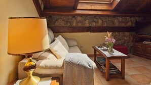 Una habitación acogedora con sofá, una mesa con lámpara, pared de piedra y televisión.