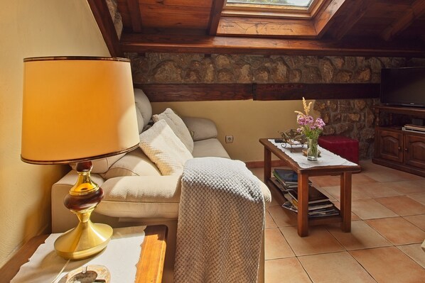 Una habitación acogedora con sofá, una mesa con lámpara, pared de piedra y televisión.
